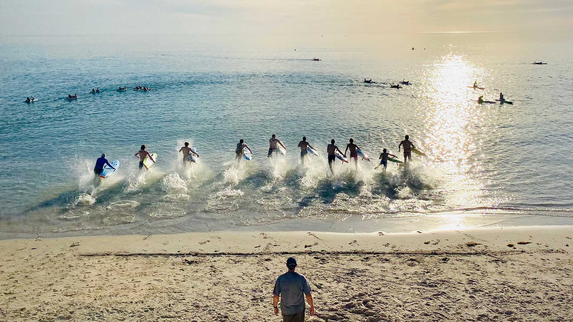 Surf lifesavers training at sunrise on West Beach in Adelaide, running from the water toward the shore.