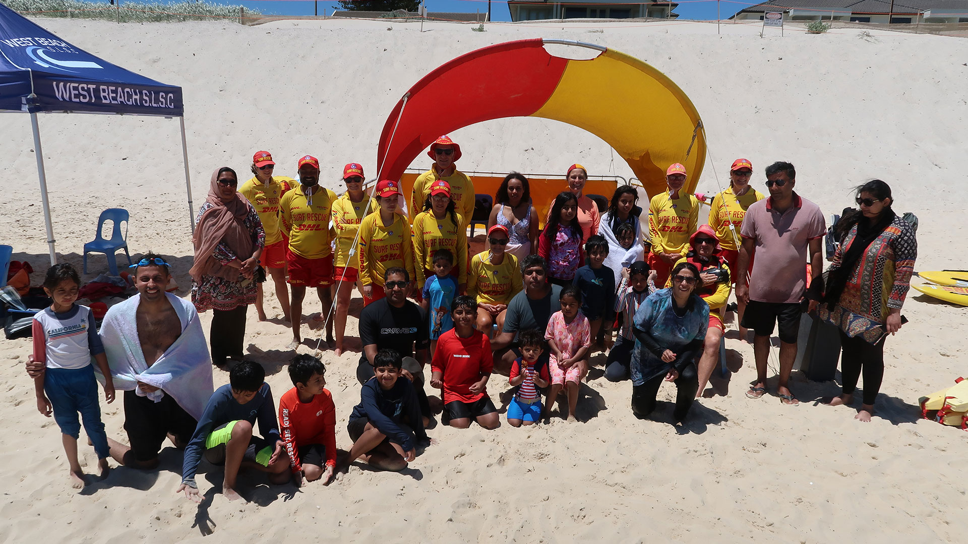 Group of Adelaide surf lifesavers and families gathered on West Beach during a West Beach SLSC community event.